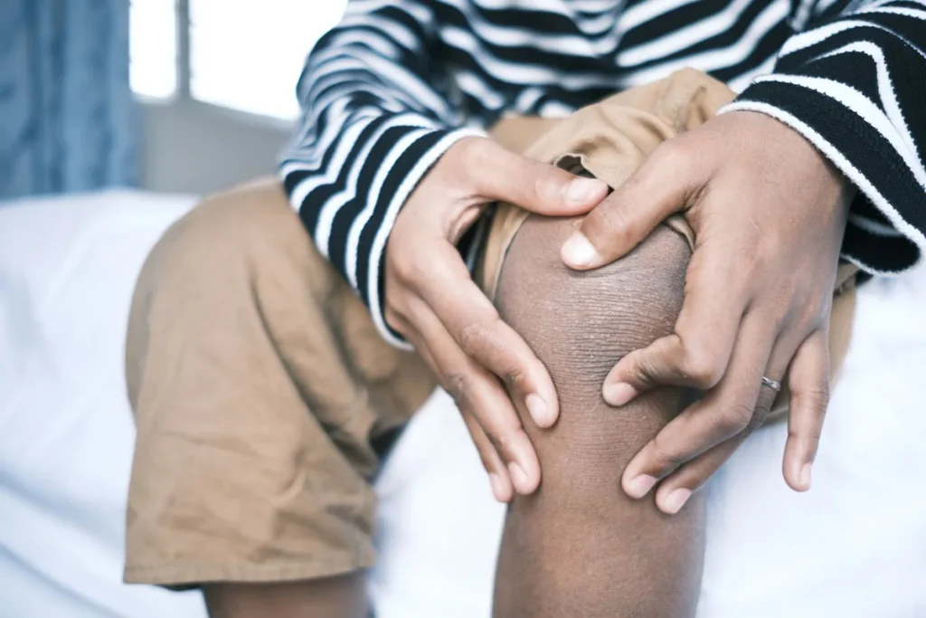 A person sitting on a bed, holding one bare knee with both hands