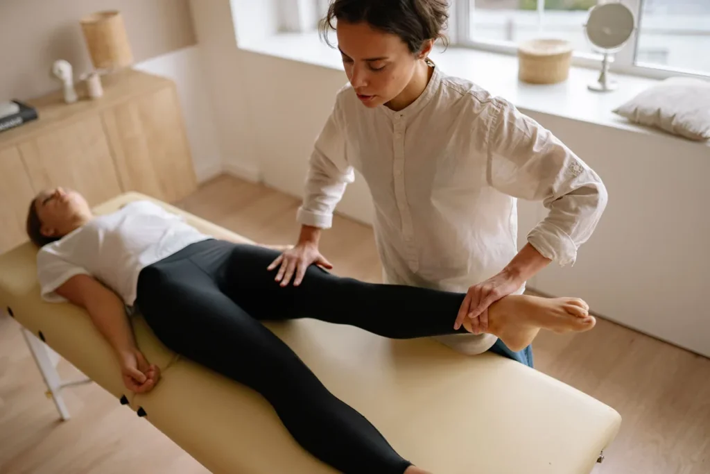 A physiotherapist holding and moving the leg of a woman lying on a treatment couch